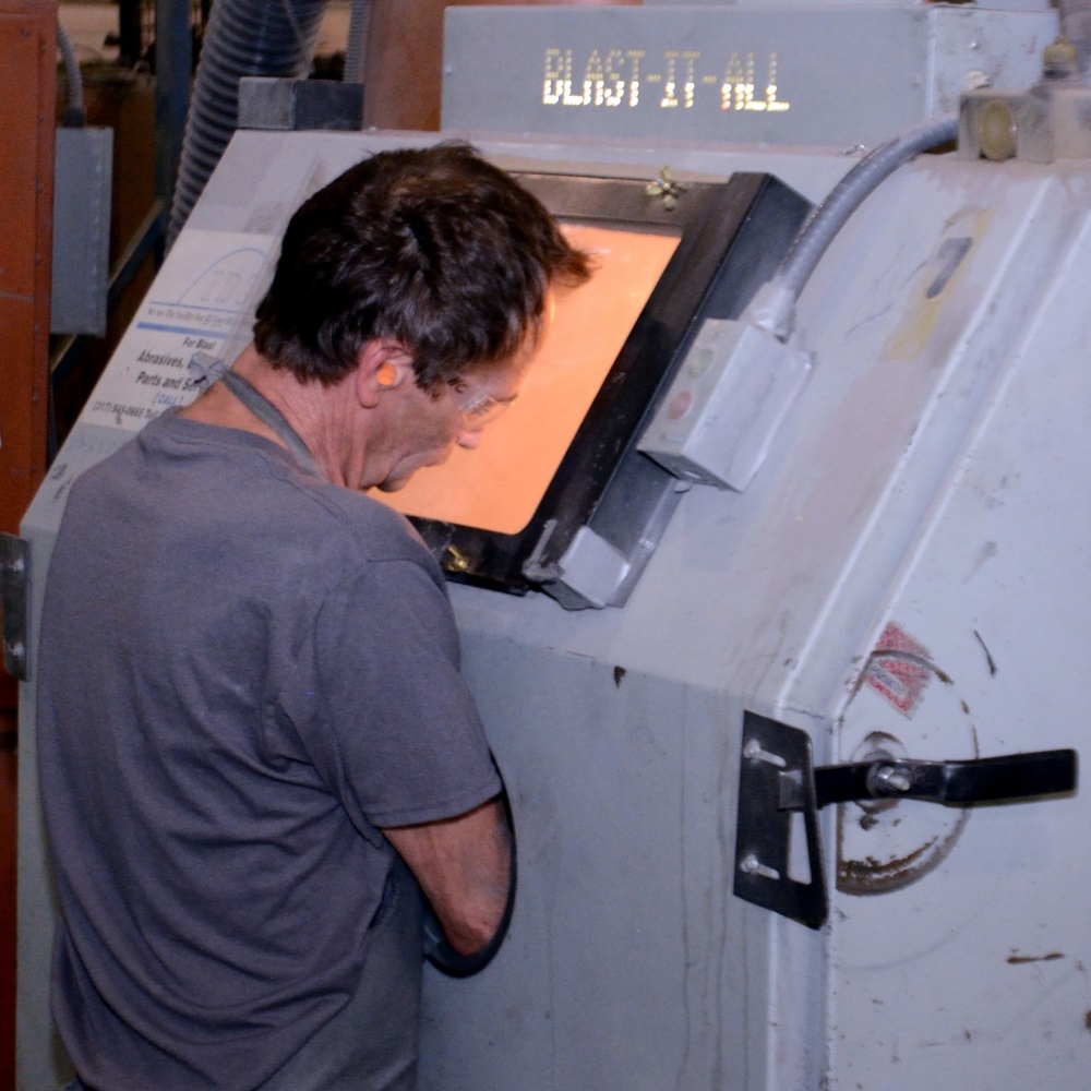 Employee using blast cabinet to prepare part for finishing
